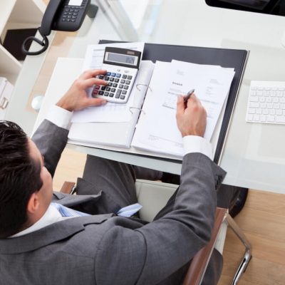 Businessman Calculating Documents Using Calculator In Office